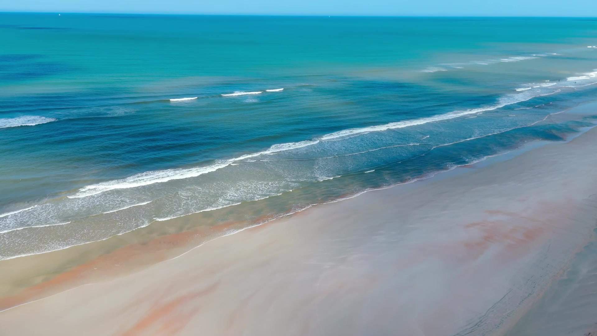 Aerial view of surf rolling onto a wide sandy beach near St. Augustine