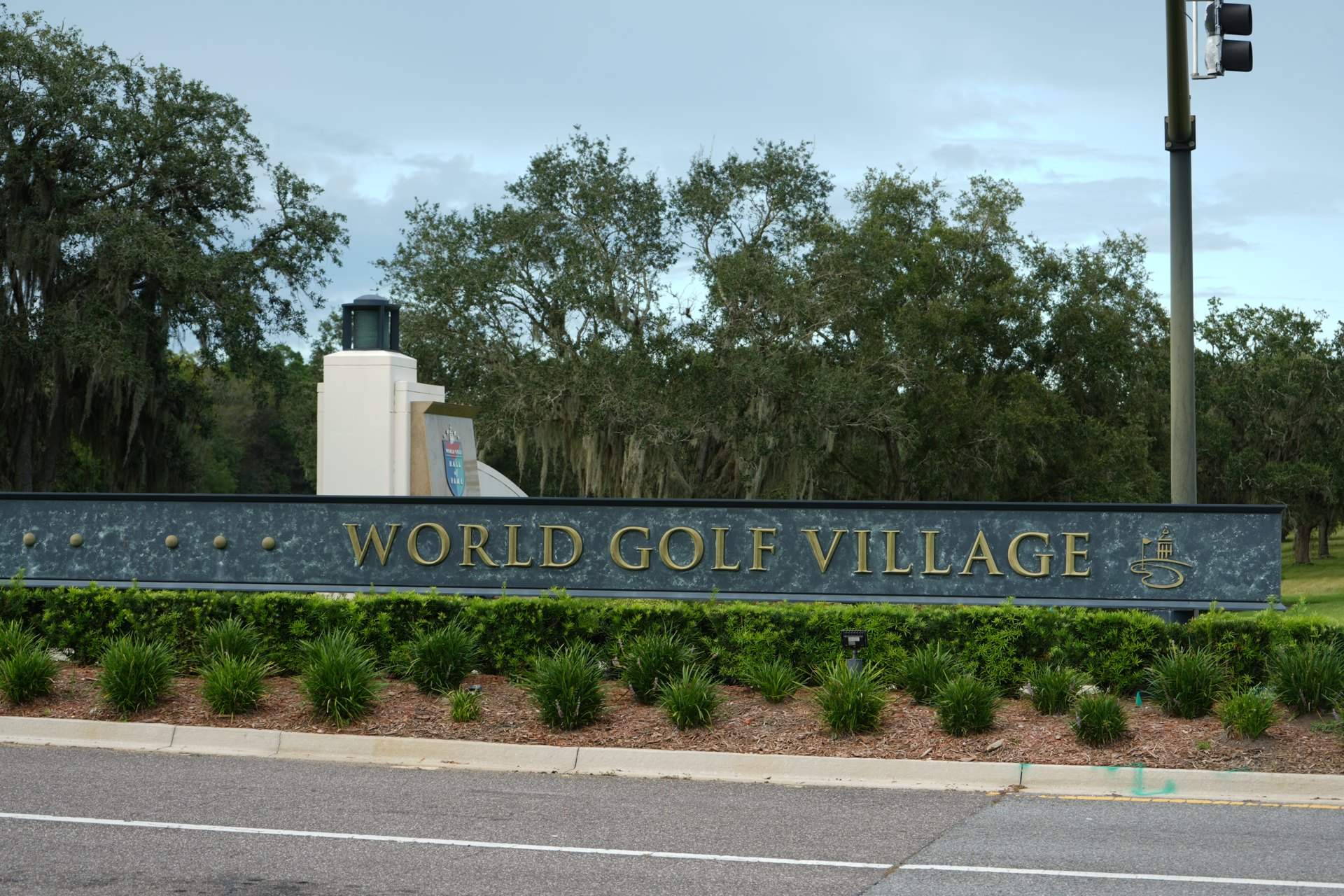 World Golf Village sign wall along the entrance road under live oaks